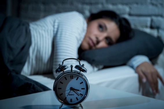 clock in foreground showing twenty past three in the early morning with lady on bed awake in the background